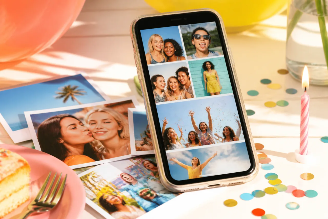 Un móvil que muestra un collage de fotos de amigos, apoyado en un escritorio luminoso junto a fotos impresas y una vela de cumpleaños